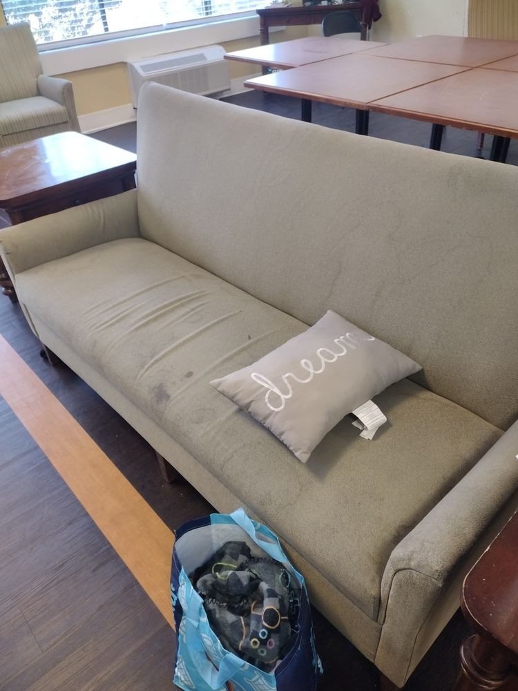 A green sofa with a decorative pillow on it in a living room setting.