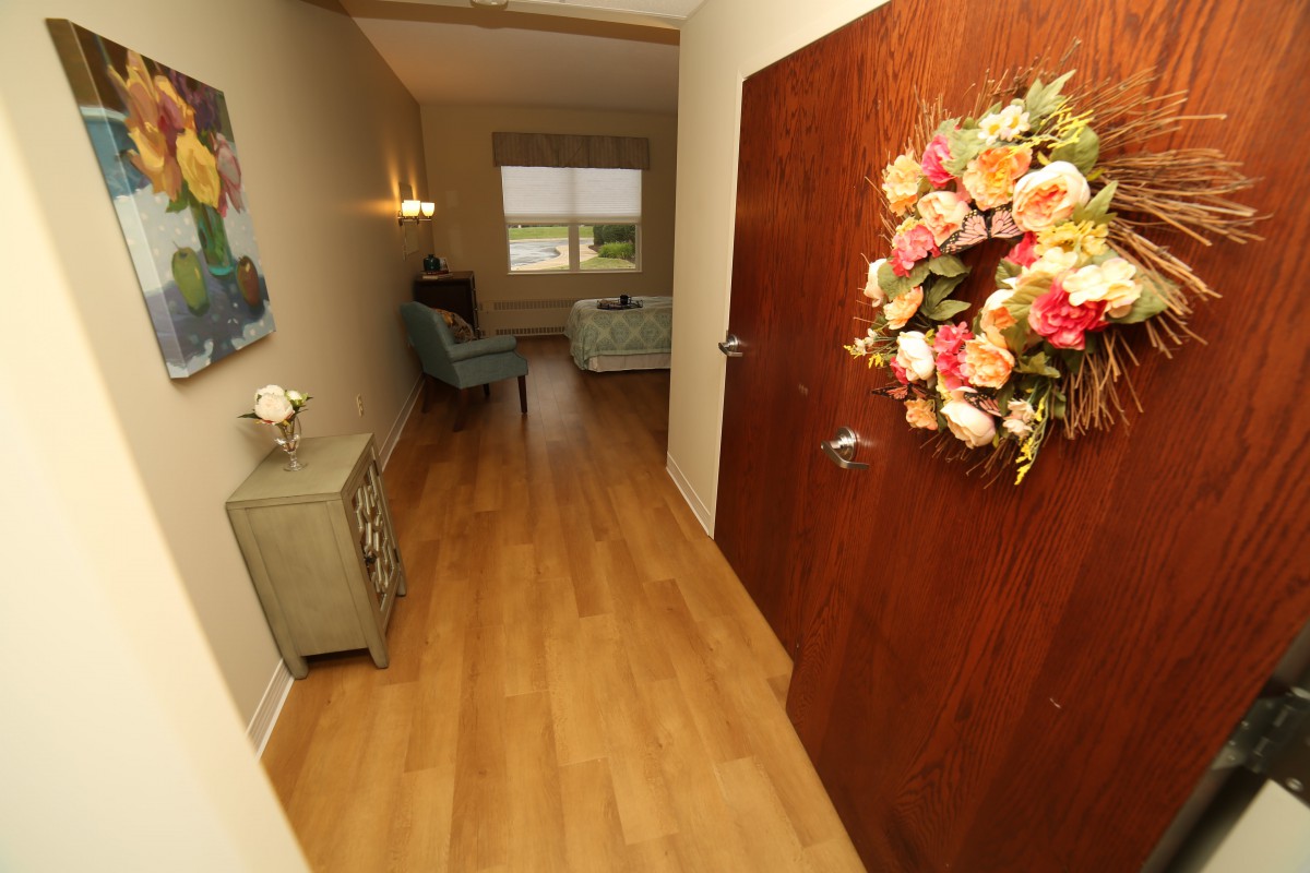 A cozy hallway with wooden flooring and floral decorations on the door, leading to a sitting area.