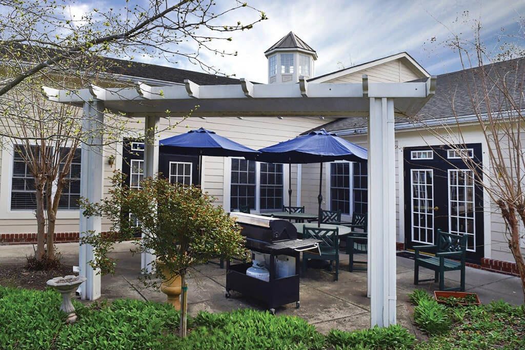 A cozy outdoor patio with a pergola, featuring blue umbrellas, seating, and a grill.