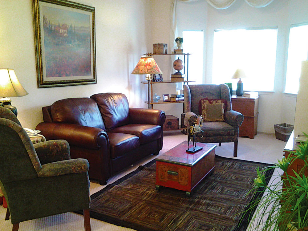 A cozy living room with leather sofas, armchairs, a coffee table, and a large window letting in natural light.