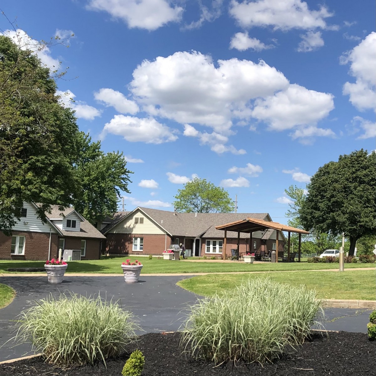 A picturesque house surrounded by trees and a well-kept yard under a sky with fluffy clouds.