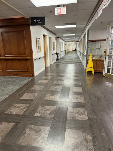 A well-lit hallway featuring wooden flooring and a caution sign, suggesting cleaning or maintenance.