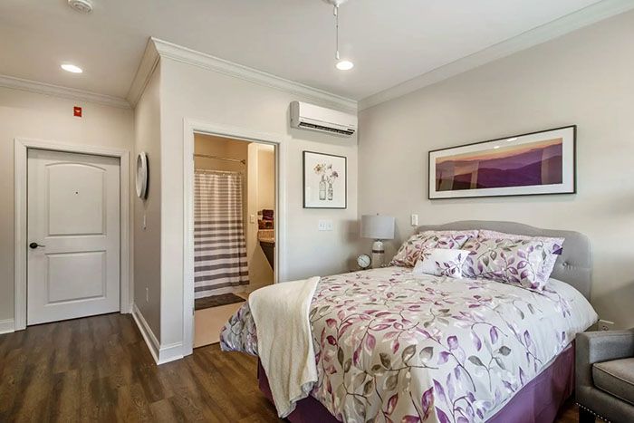A modern bedroom with floral bed linens, artwork on the wall, and an air conditioner.