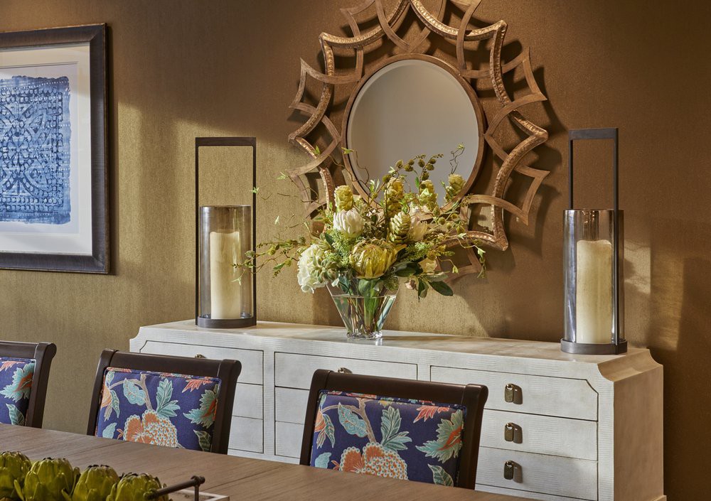 A beautifully decorated dining room featuring an ornate mirror, floral arrangement, and elegant candles on a sideboard.