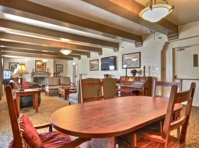 A cozy living room interior with a wooden table and chairs, featuring beamed ceilings and elegant lighting.