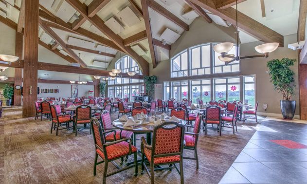An elegant dining area with wooden beams and large windows, set up with tables and chairs.