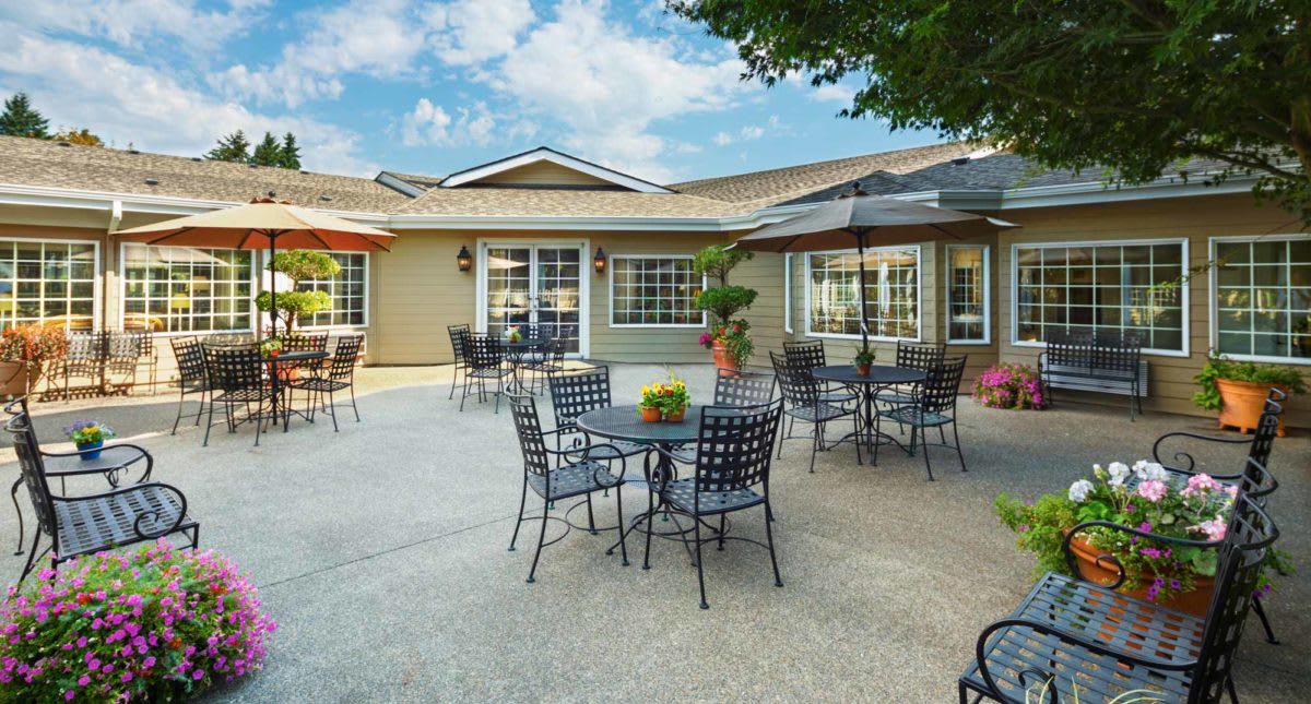 A well-furnished outdoor patio with tables, chairs, and umbrellas set against a building, ideal for relaxation under a clear sky.