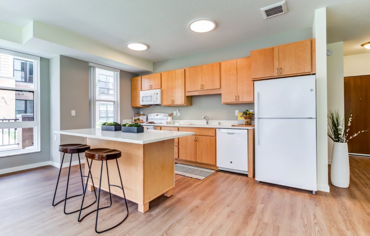 A modern kitchen featuring wooden cabinets, an island with stools, and essential appliances.