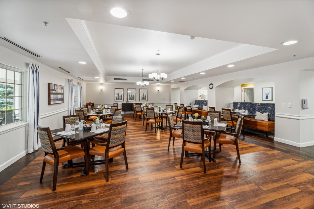 A spacious dining room with neatly arranged tables and chairs on a polished hardwood floor, illuminated by elegant chandeliers.