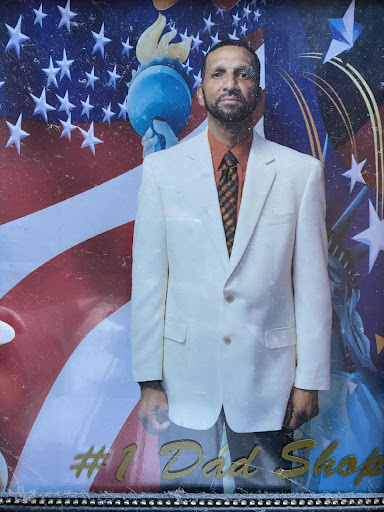 A man dressed in a stylish white suit stands against a vibrant background featuring the American flag.