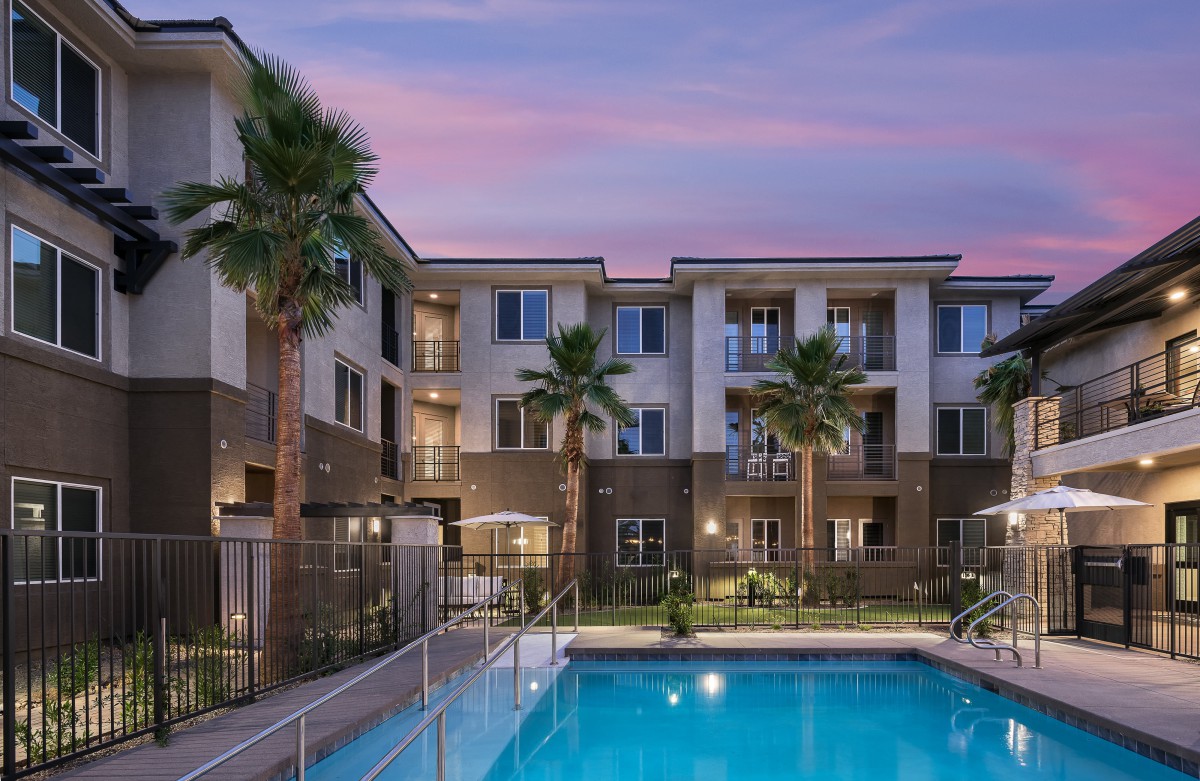 A well-lit apartment complex with a swimming pool and palm trees at dusk.