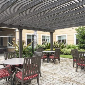 A cozy outdoor patio area with tables and chairs under a pergola, surrounded by well-maintained landscaping.