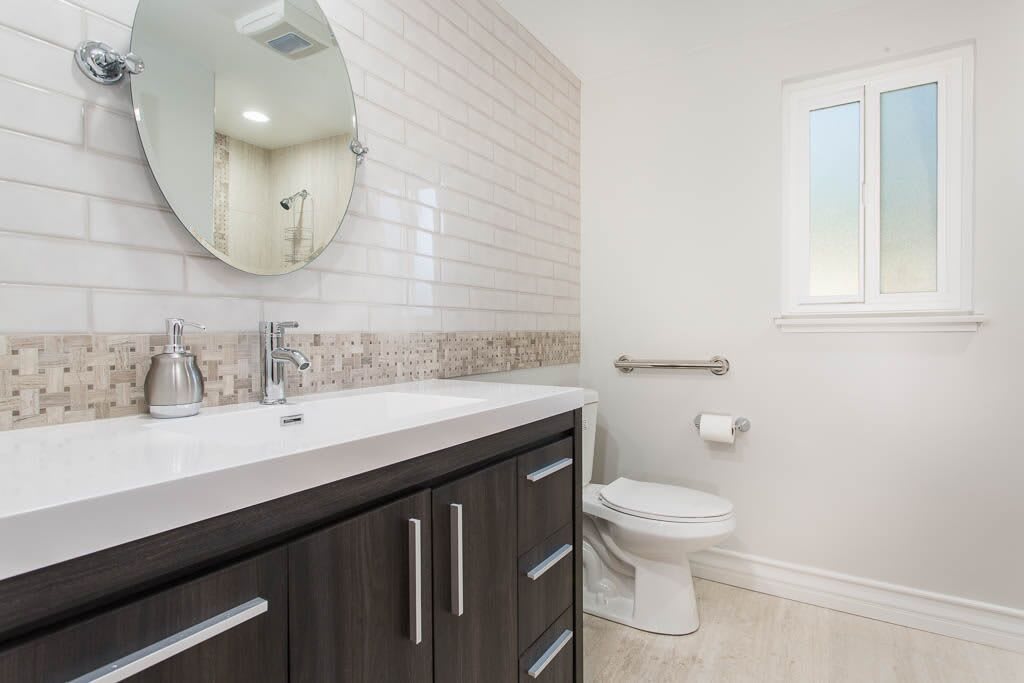 A modern bathroom featuring a sink with dark cabinetry, a large mirror, and white tiled walls.