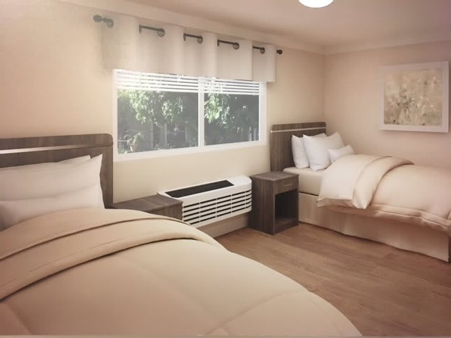 A modern bedroom with two neatly made beds, a large window with curtains, and an air conditioning unit below.
