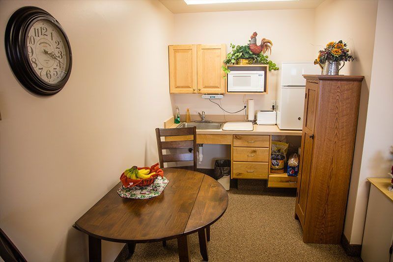 A cozy kitchenette with a round table and chairs, featuring a fruit bowl and wooden cabinets.