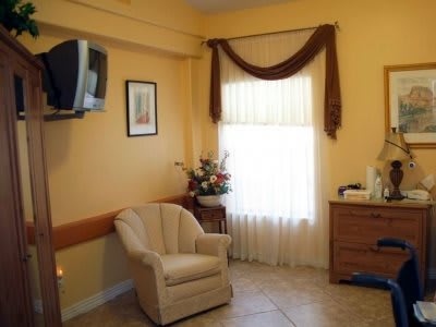 A cozy living room interior featuring a comfortable chair, a window with curtains, and a mounted television.