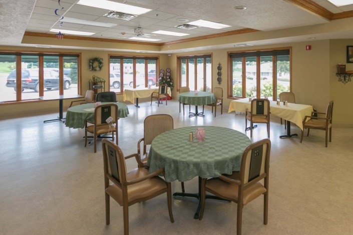 A spacious dining hall with round tables and chairs, illuminated by natural light from large windows.