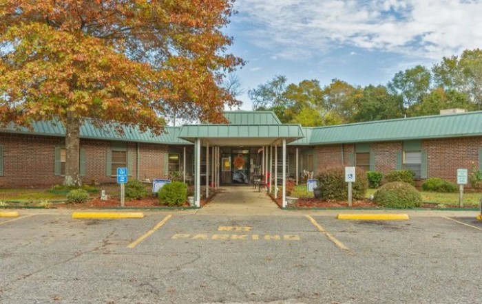 A brick building with a green roof surrounded by autumn trees and a parking lot.