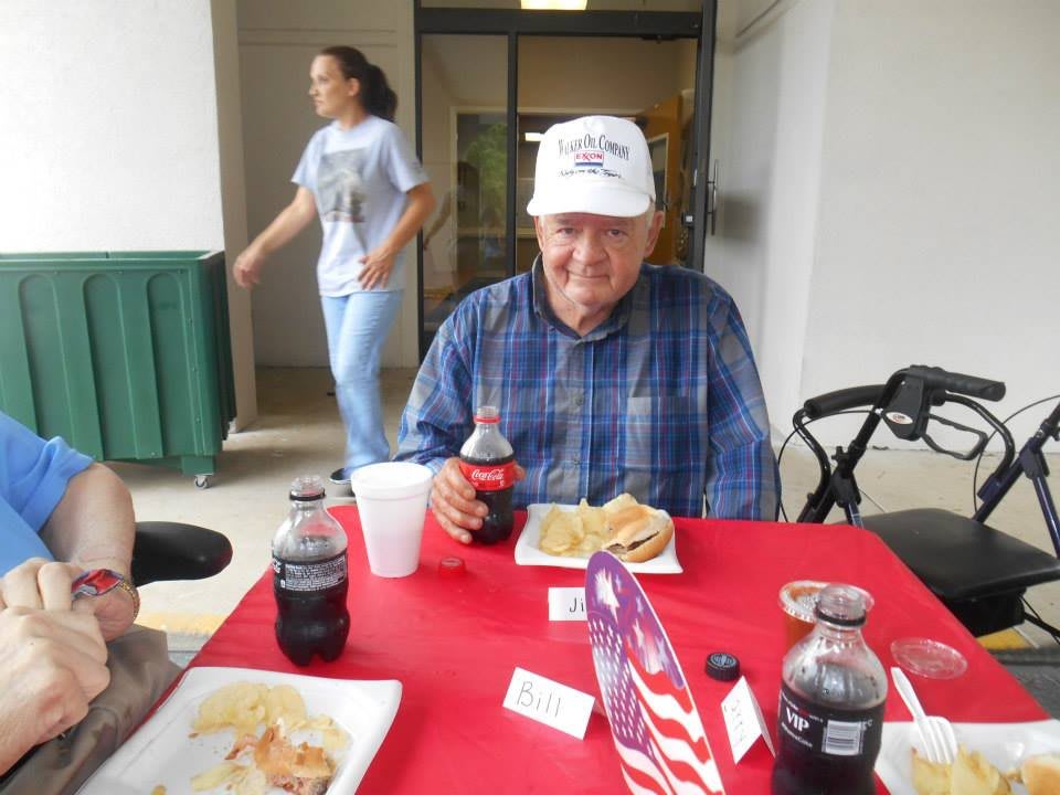 A man sitting at a table with food and drinks, wearing a plaid shirt and a hat.