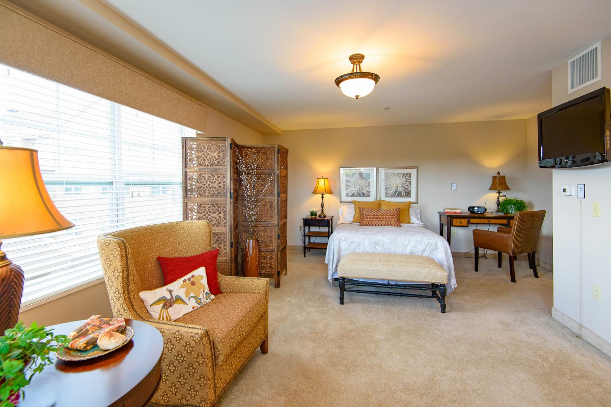 A cozy bedroom with warm lighting, featuring a comfortable armchair, a bed with decorative pillows, and elegant decor.
