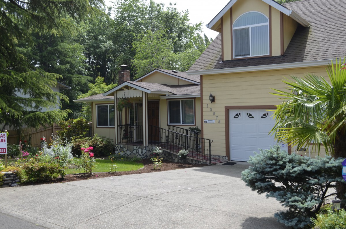 A charming residential house with a driveway and garage, surrounded by trees and a front yard.