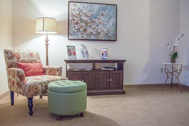 A cozy living room corner featuring a floral artwork, comfortable chair, and decorative lamp.