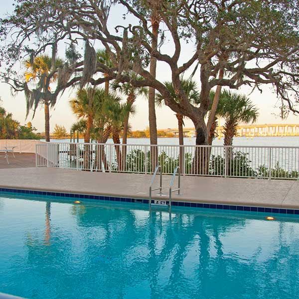 A serene outdoor pool with a backdrop of trees and waterfront views.