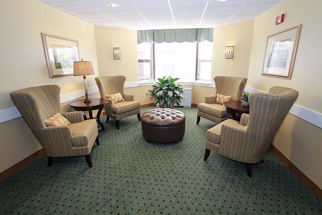 A cozy seating area with upholstered chairs and a central ottoman, decorated with warm lighting and a potted plant.