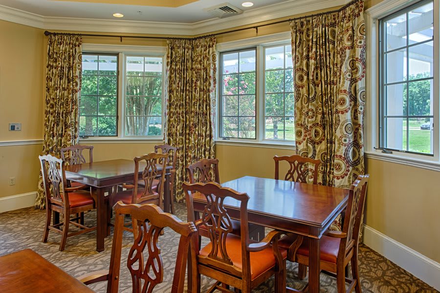Elegant dining room with wooden tables and chairs, complemented by patterned curtains and large windows.