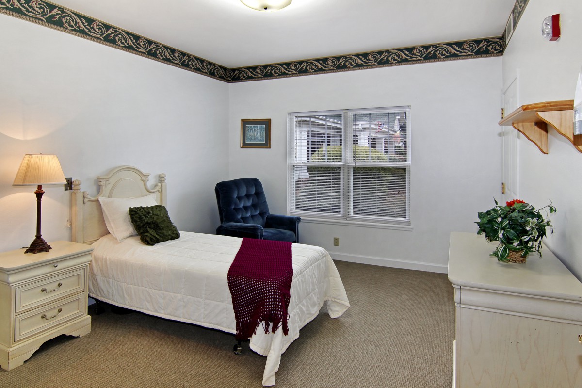 A cozy bedroom with a single bed, an upholstered chair, and a window letting in natural light.
