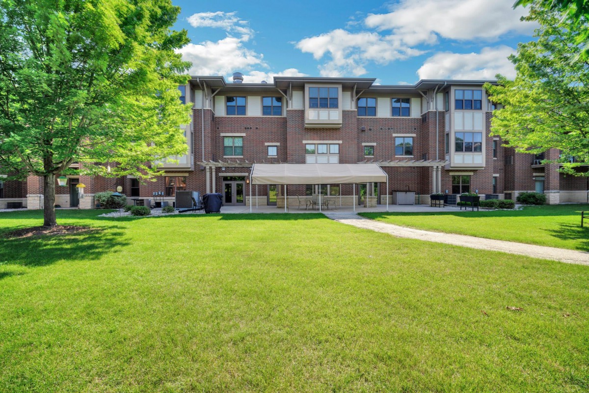 A three-story brick building with a grassy lawn, trees, and a clear sky in the background.