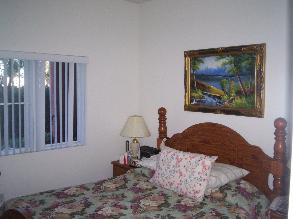 A cozy bedroom with a bed, lamp, window, and wall painting.