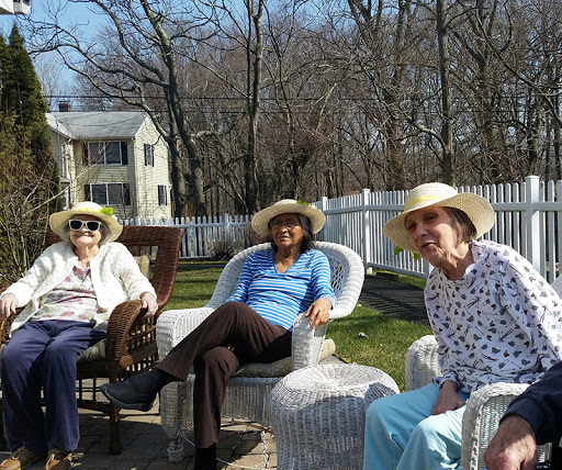 Three elderly women enjoy a sunny day outdoors, dressed in hats and relaxed in their chairs.