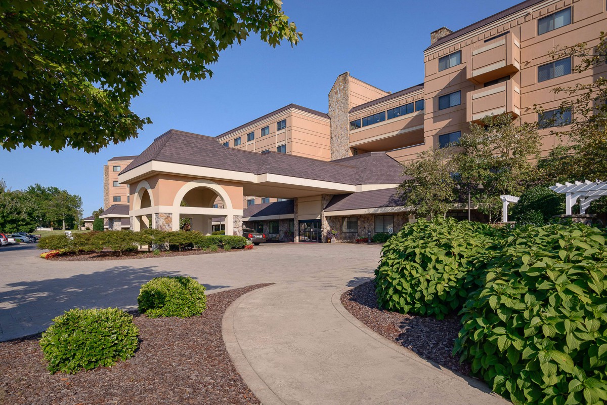 The entrance of a hospital building surrounded by well-maintained landscaping on a sunny day.