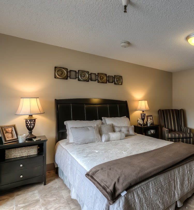 A cozy bedroom with neutral tones, featuring a large bed, bedside tables with lamps, and decorative wall art.