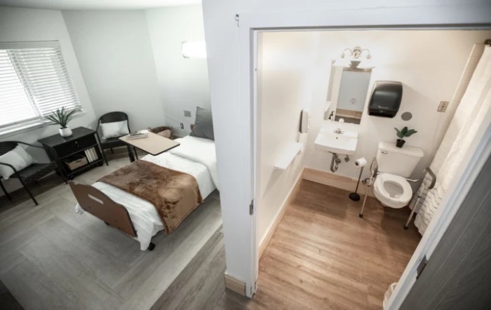 A hospital room with an adjoining bathroom, featuring a patient bed and medical equipment.