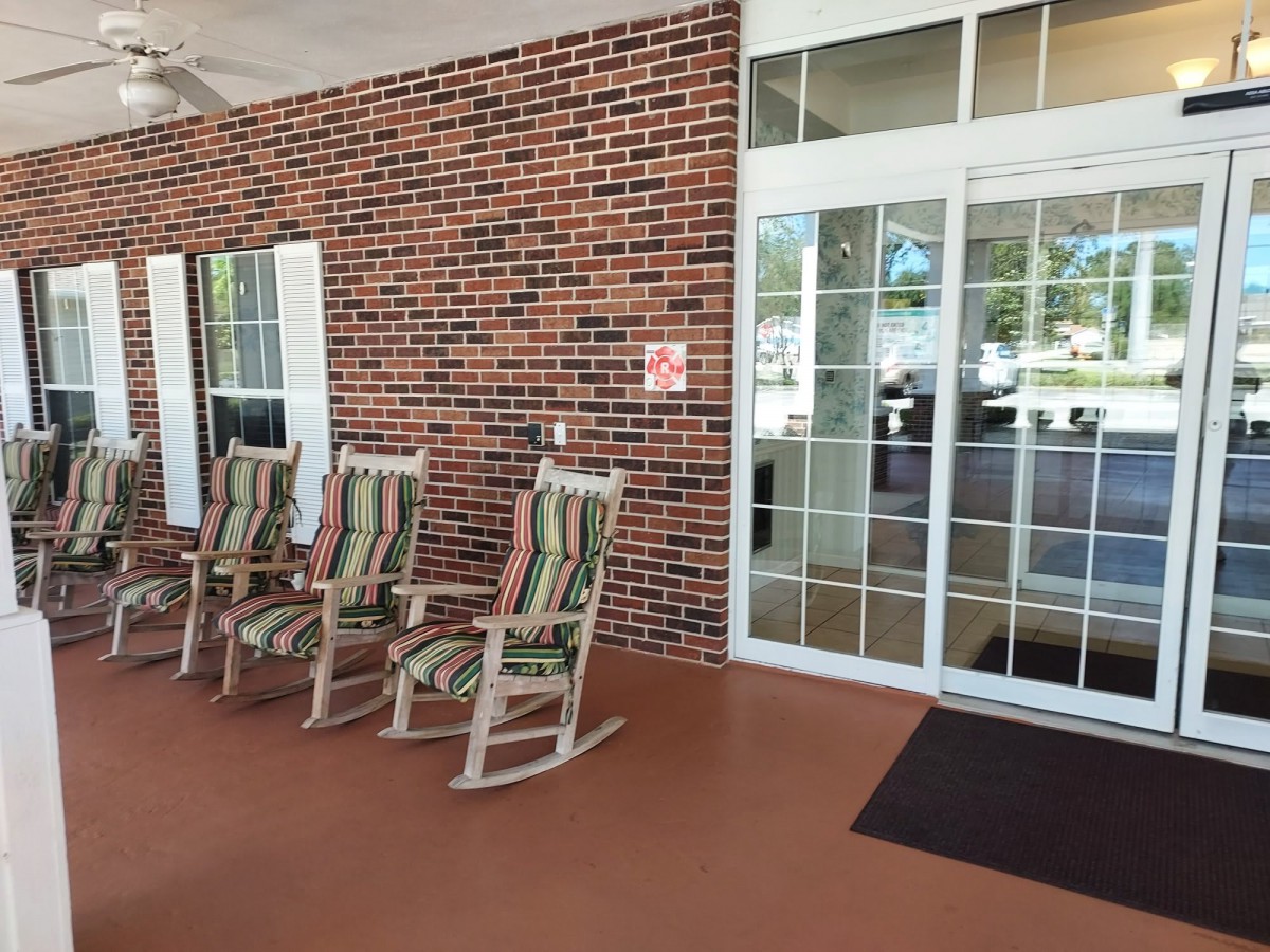 A cozy porch area with three rocking chairs facing a brick wall and glass entrance.