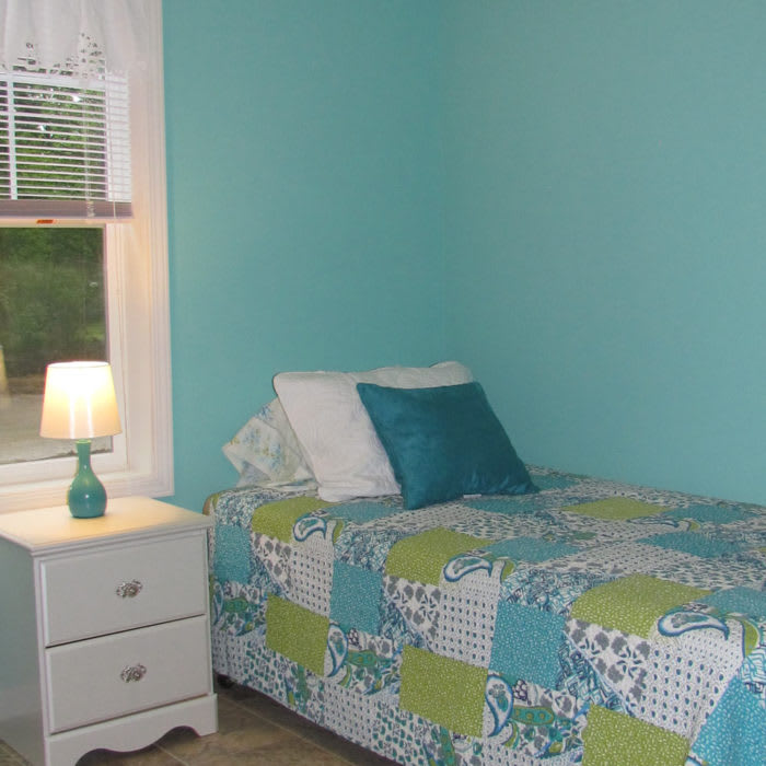 A cozy bedroom with a single bed, colorful bedding, and a lamp on the nightstand.
