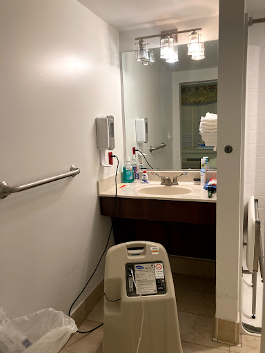 A view of a bathroom featuring a sink, mirror, and various cleaning supplies.