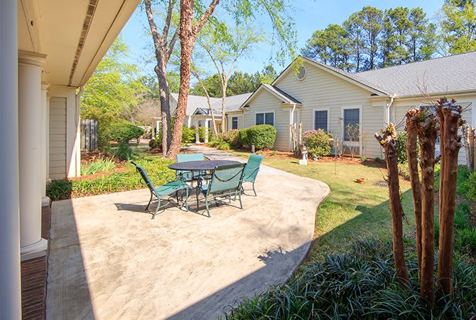 A sunny patio with a table and chairs, surrounded by a garden and trees.