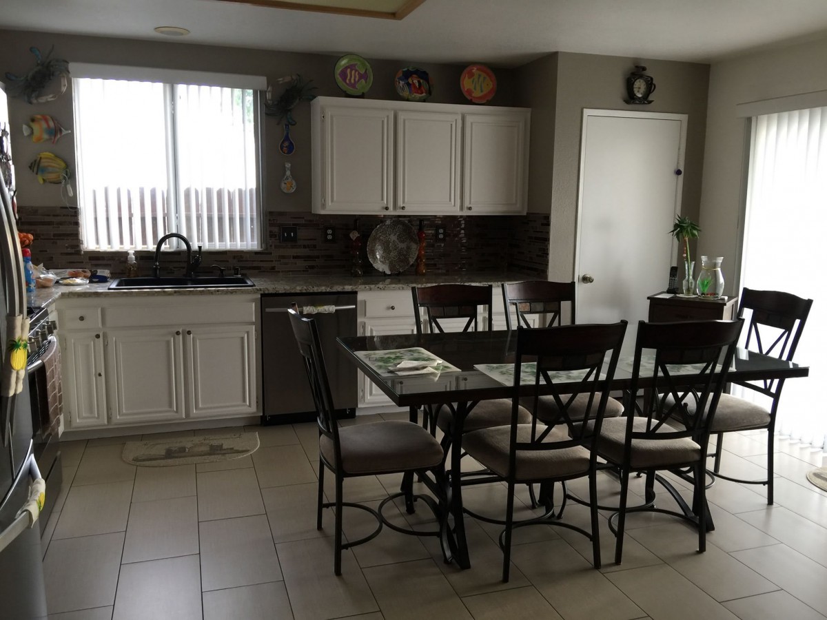 A modern kitchen with a dining table and chairs, featuring white cabinets and a tiled floor.