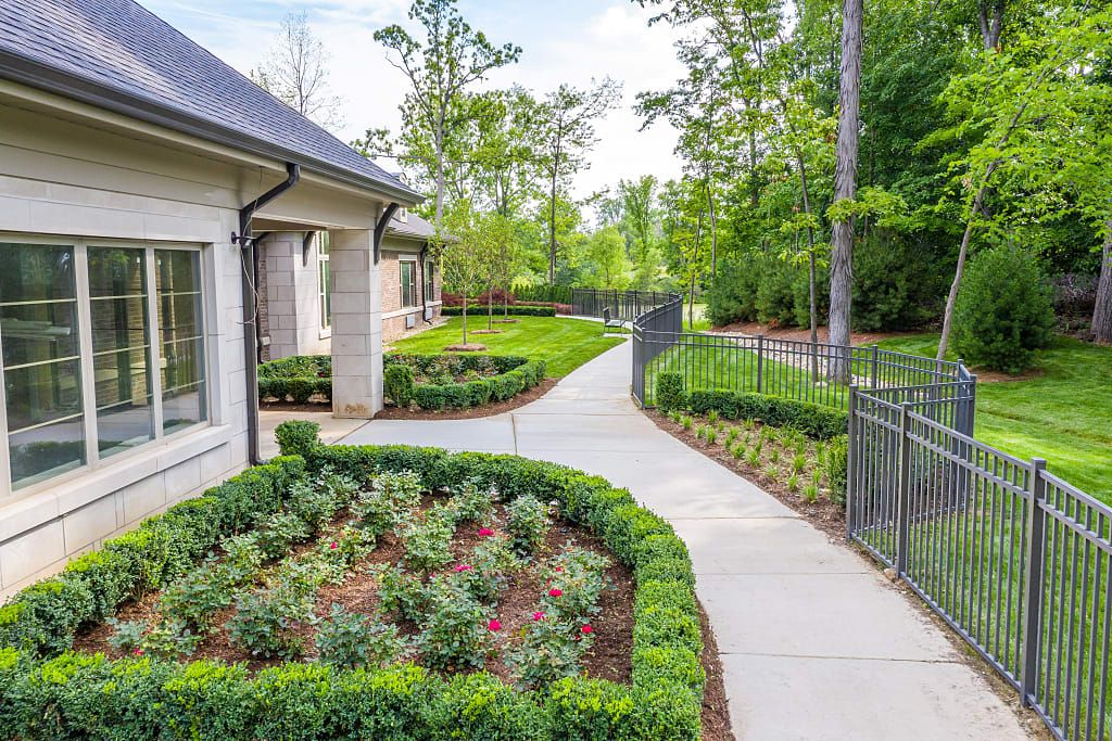 A well-maintained garden with a pathway surrounded by lush greenery and a house in the background.
