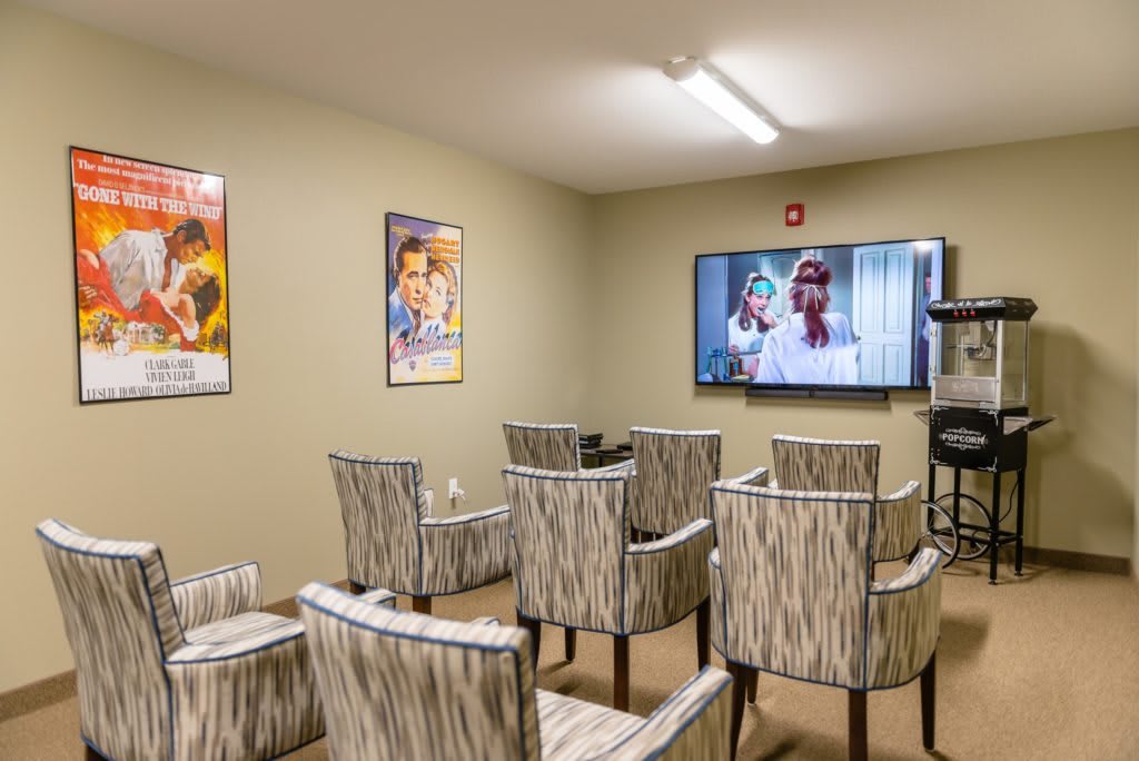 A cozy home theater room with neatly arranged chairs, a large screen displaying a movie, and film posters adorning the walls.
