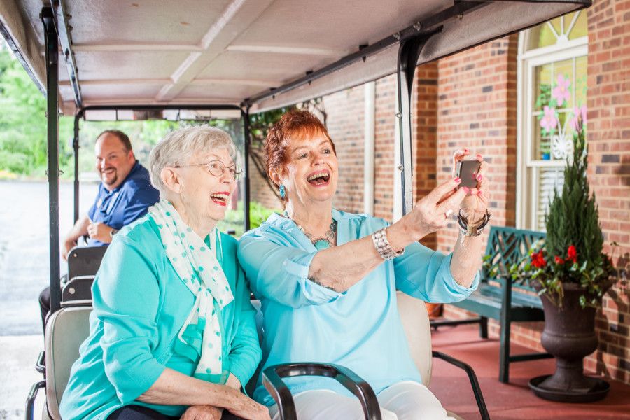 Two senior women enjoying a selfie together while smiling and sitting indoors.
