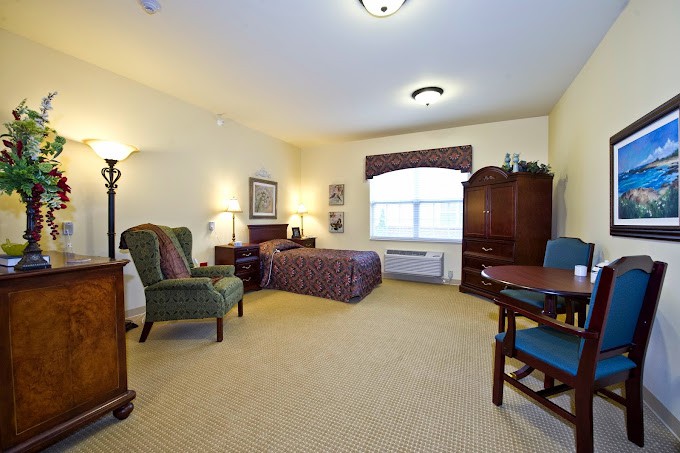 A spacious and well-furnished hotel room featuring a bed, armchair, wooden furniture, and ample lighting.
