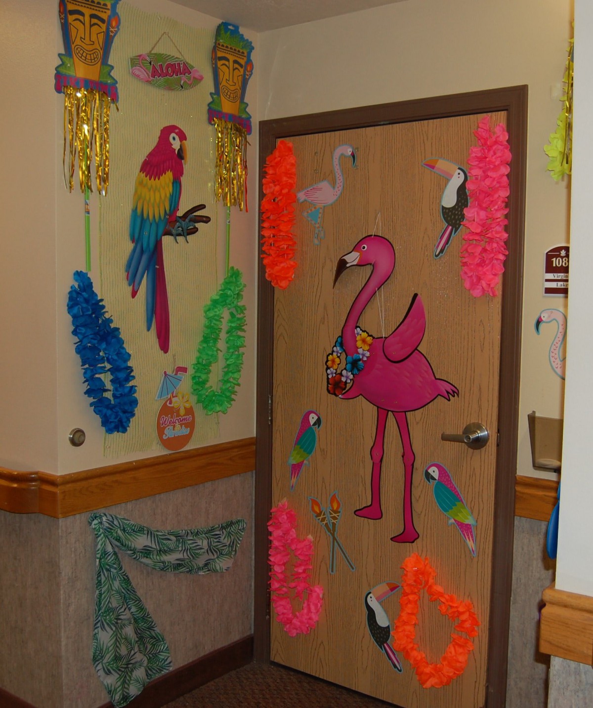 A tropical-themed door decorated with a pink flamingo, colorful parrots, and vibrant leis.