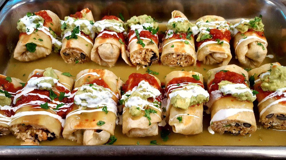A tray of baked chimichangas topped with guacamole, sour cream, and salsa.