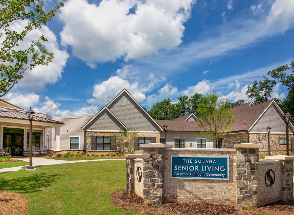 A senior living facility surrounded by a well-maintained lawn and trees under a partly cloudy sky.