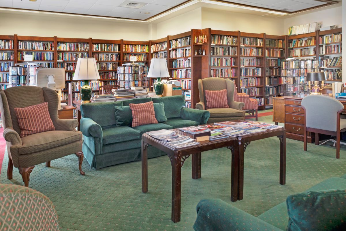 A cozy library with armchairs and sofas surrounded by bookshelves.