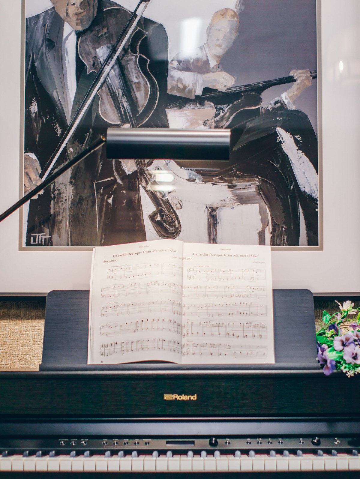 A piano with an open sheet of music, illuminated by a lamp, with artwork in the background.